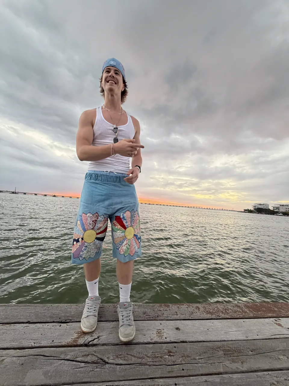 Washed-out blue drawstring shorts with Dresden-plate quilt flowers on each leg, worn on a pier at sunset