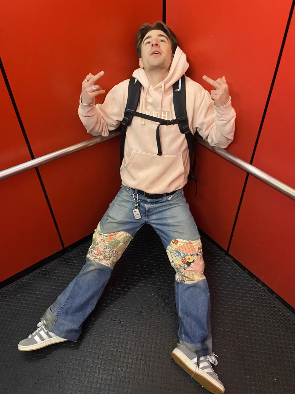 Mid-wash jeans with both knees rebuilt in floral quilt patches, worn in a red elevator