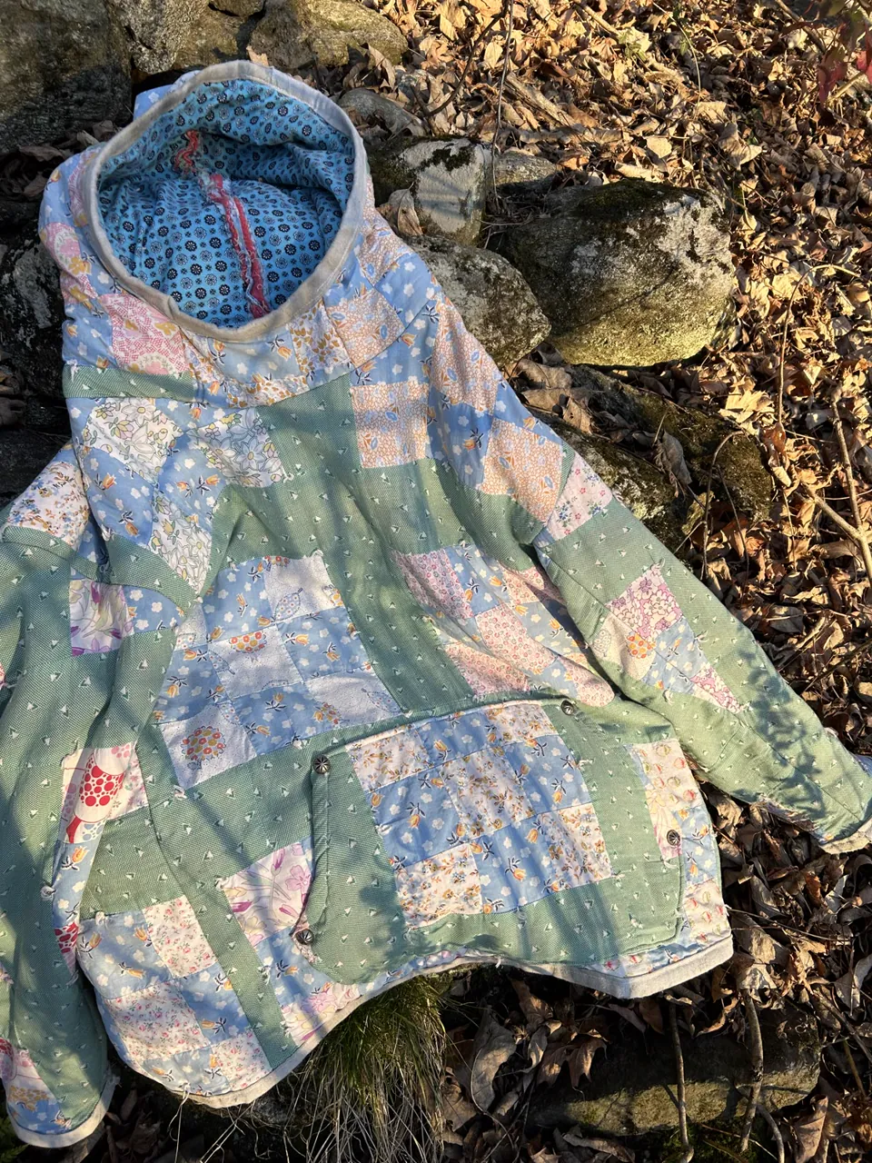 Quilt hoodie in seafoam green and blue calico lying on a stone wall in low sun