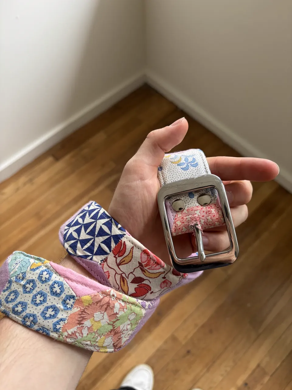 A second patchwork belt wrapped around a wrist, chrome buckle in the palm